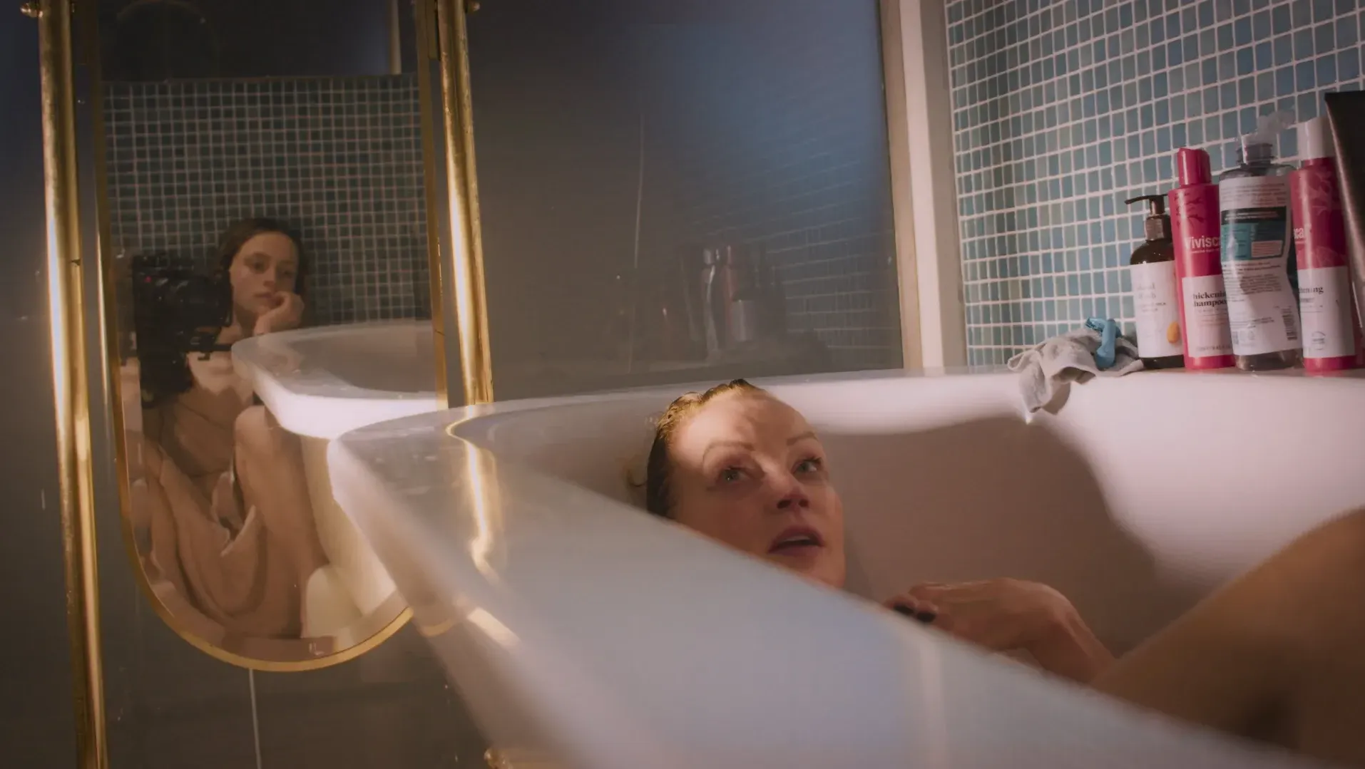 Louise is in  the bath, we can see Meg filming her in the reflection in the mirror. They are talking