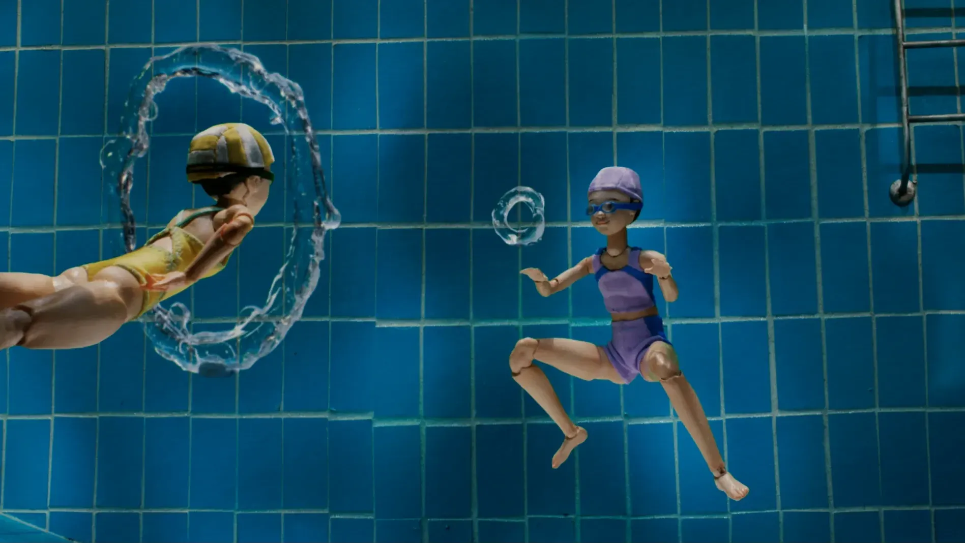 Two girls underwater: one blows bubble rings while the other reaches out to pass through them